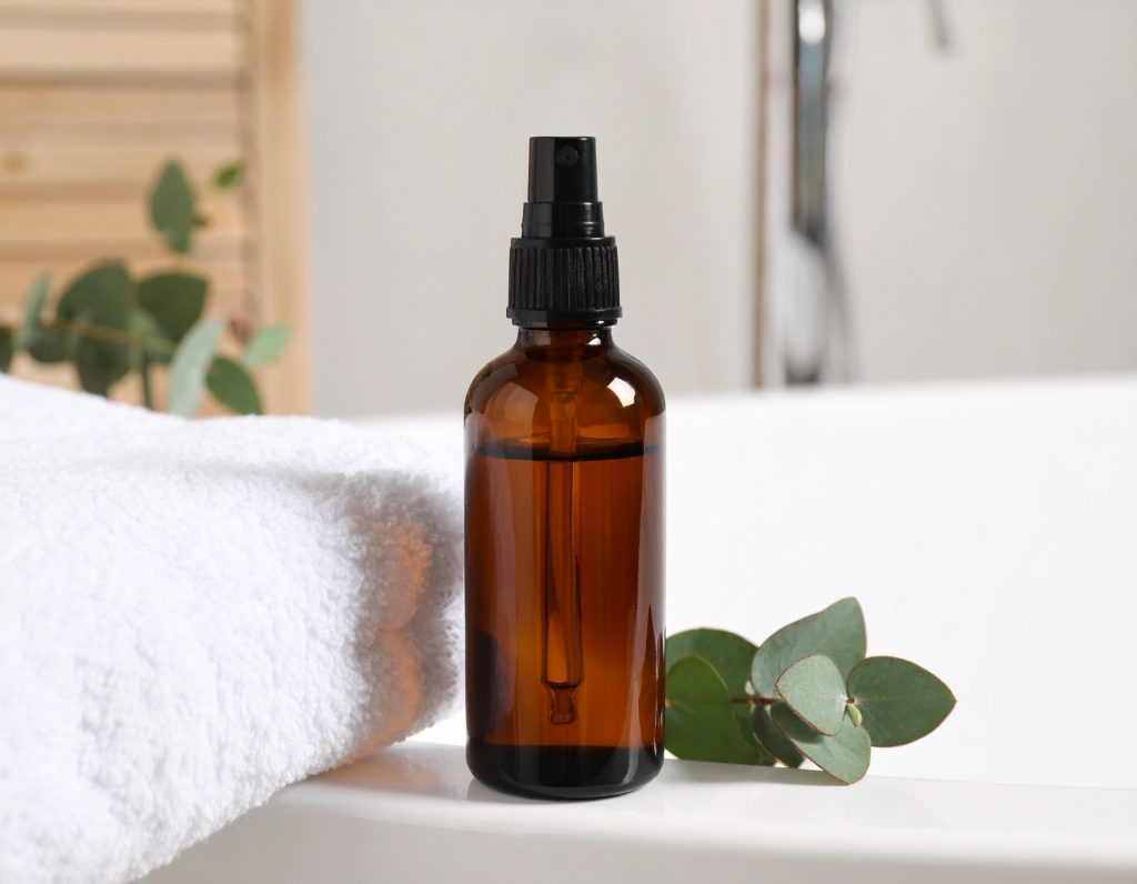 Natürlicher Schimmelreiniger aus Alkohol und Teebaumöl in einer Glasflasche – neben Eukalyptusblättern und Baumwolltuch in einem minimalistischen Badezimmer.